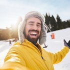 Selfie of a happy young Caucasian in the snow wearing a yellow jacket and raising one hand